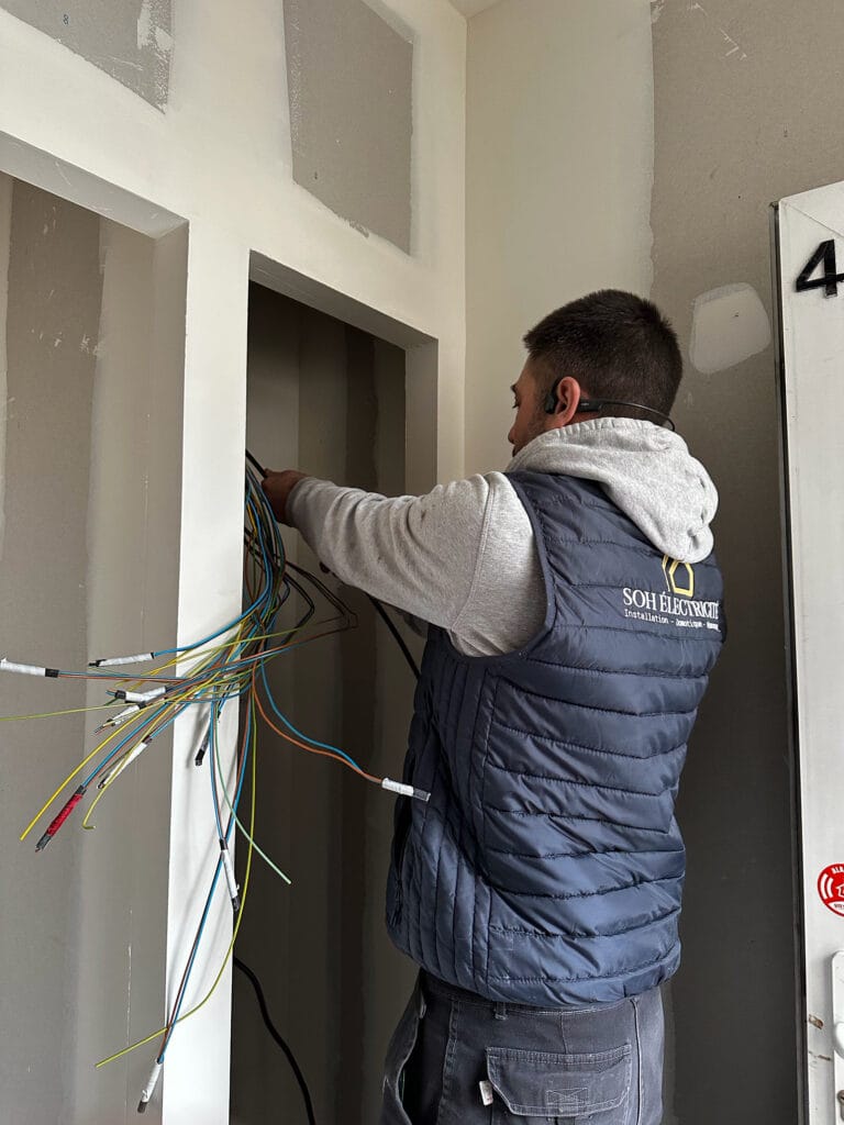 Électricien de SOH Rénovation en blouson de l’entreprise, en train de raccorder des câbles électriques lors d’une intervention